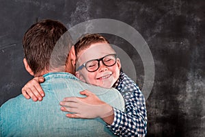 Little boy resting on her father's shoulder. Little son hugging his dad near wal. Happy father and child boy on hands