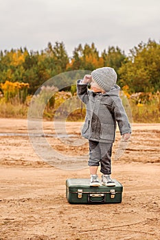 Little boy in retro gray clothes climbed on an old suitcase in search of