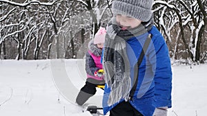 Little boy rides a girl on a sled in winter in a snow-covered forest