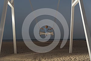 Little boy rides high in the sky on rope swing on sea background. Dark blue skies at twilight