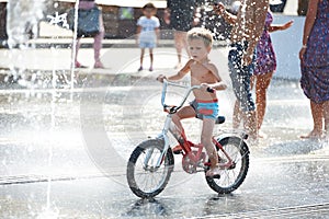 Little boy rides his bike among fountains