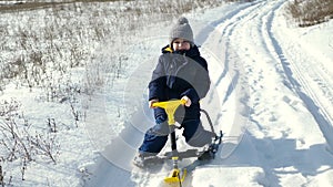 Little boy rides a sled, a snowmobile in a snowy forest