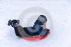 A little boy rides a sled from a winter slide