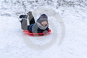 A little boy rides a sled from a winter slide