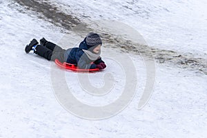 A little boy rides a sled from a winter slide