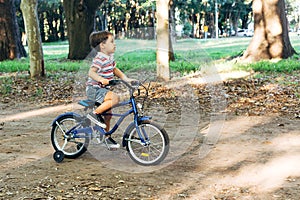 Little boy riding a blue bike in a dirty road in a forest park. Bicycle with the training wheels.