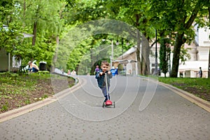 Little boy riding scooter in city park in aummer. Kids sports outdoors. Happy child playing with his scooter. Kid learn to ride