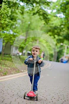 Little boy riding scooter in city park in aummer. Kids sports outdoors. Happy child playing with his scooter. Kid learn to ride