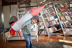 A little boy with a rocket toy on his back enjoys posing while playing at home. Home, game, childhood