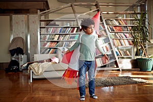 A little boy with a rocket toy on his back is having fun at home while imagining flying to the space. Home, game, childhood