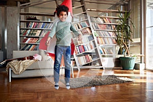 A little boy with a rocket toy on his back is jumping while playing at home. Home, game, childhood