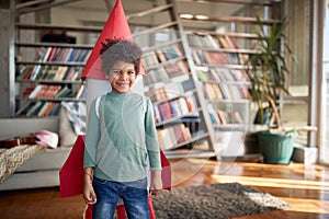 A little boy with a rocket toy on his back is posing while playing at home. Home, game, childhood