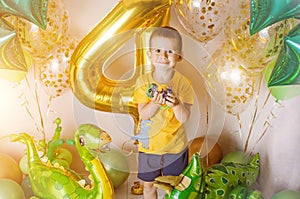 Little boy in room decorated for birthday party with baloons, large inflatable number 4, Dinosaur baloons