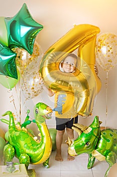 Little boy in room decorated for birthday party with baloons, large inflatable number 4, Dinosaur baloons