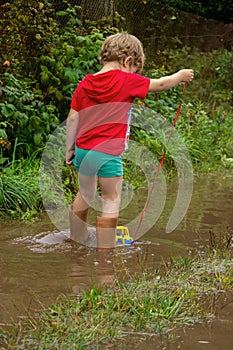 Little boy in rubber boots pulls a toy toy car tractor on a rope