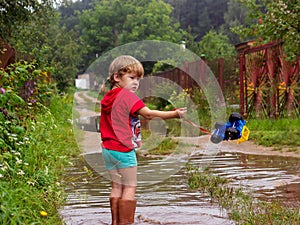 Little boy in rubber boots pulls a toy toy car tractor on a rope