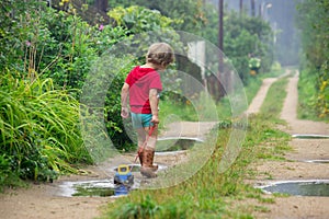 Little boy in rubber boots pulls a toy toy car tractor on a rope