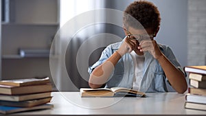 Little boy rubbing tired from active reading eyes, doing lots homework, studying