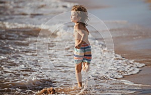 Little boy running on beach shore splashing water in blue sea. Kid walking the summer beach.