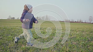 Little boy running on the grass in the field at sunset, slow motion.