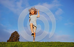 Little boy running and jumping on the grass near a spring green meadow on blue sky. Happy child girl playing on sunny