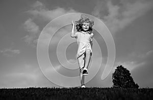 Little boy running and jumping on the grass near a spring green meadow on blue sky. Happy child girl playing on sunny