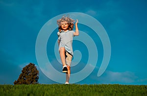 Little boy running and jumping on the grass near a spring green meadow on blue sky. Happy child girl playing on sunny