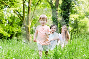 Little boy running over meadow with family in back