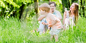 Little boy running over meadow with family in back