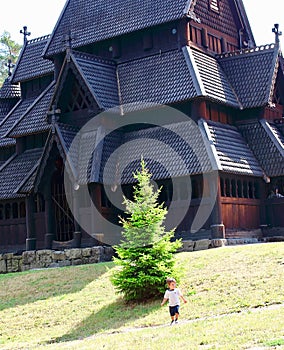 Little boy running and playing in front of the Gol Church, a stave church originally built in Gol city, now in Oslo.