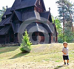 Little boy running and playing in front of the Gol Church, a stave church originally built in Gol city, now in Oslo.