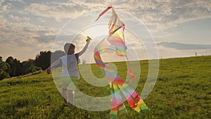 Little boy running playing with a kite in the meadow at sunset
