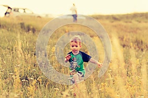 Little boy runs across the field through the grass at sunset