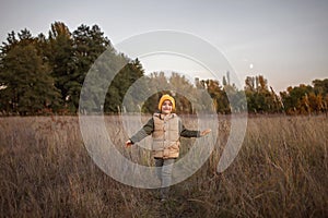 Little boy runs alone path through a dry meadow over beautiful autumn forest background