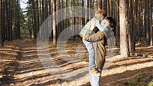 A little boy runs along the road against the background of the forest. The mother takes the child in her arms and hugs