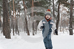 Little boy runs merrily through snow. Child plays in winter forest on large fir trees background