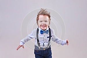 The little boy runs and smiles, wearing a blue bow tie and suspenders