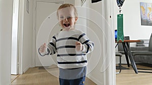 Little boy's feet in slow motion as he runs across the wooden floor of a long corridor in his house. Joyous childhood.