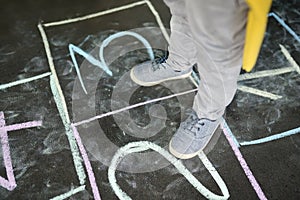 Little boy`s jump on hop scotch drawn on asphalt. Child playing hopscotch game on playground outdoors on a sunny day