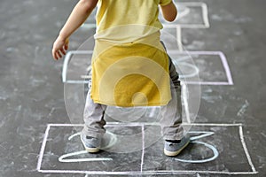 Little boy`s jump on hop scotch drawn on asphalt. Child playing hopscotch game on playground outdoors on a sunny day