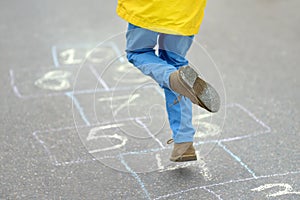 Little boy`s legs and hopscotch drawn on asphalt. Child playing hopscotch game on playground on spring day