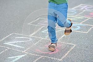 Little boy`s legs and hopscotch drawn on asphalt. Child playing hopscotch game on playground on spring day