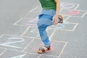 Little boy`s legs and hopscotch drawn on asphalt. Child playing hopscotch game on playground on spring day