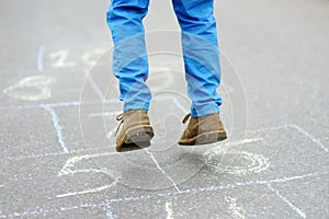 Little boy`s legs and hopscotch drawn on asphalt. Child playing hopscotch game on playground on spring day