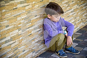 Little boy sad sitting alone at school hides his face. Isolation and bullying concept. Kid sad and unhappy, child was crying,