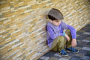 Little boy sad sitting alone at school hides his face. Isolation and bullying concept. Kid sad and unhappy, child was crying,