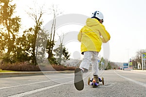 Little boy in safety helmet riding a push scooter on a spring day in public park. Quality protect equipments for safety kids on