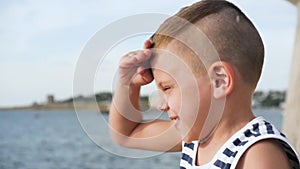 Little boy in sailor stripes shirt squint looks into the distance on sky and sea background