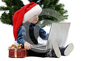 Little boy in Santa Claus cap with a laptop and Christmas gift