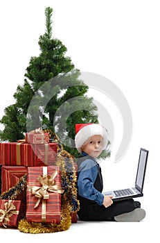 Little boy in Santa Claus cap with a laptop and Christmas gifts